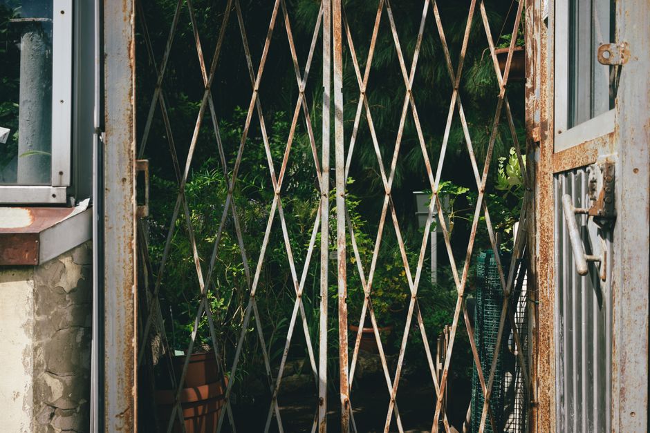 Close-up view of a black padlock securing a green wooden garden gate with vertical panels. The padlock is attached to a metal latch mounted on the gate, with the shackle showing signs of rust and corr